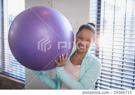 Portrait of smiling young female doctor holding purple exercise ball Portrait of smiling young female doctor holding purple exercise ball 34366715