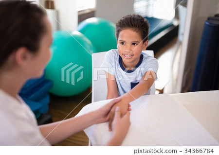 High angle view of smiling boy looking at female therapist examining hand High angle view of smiling boy looking at female therapist examining hand 34366784