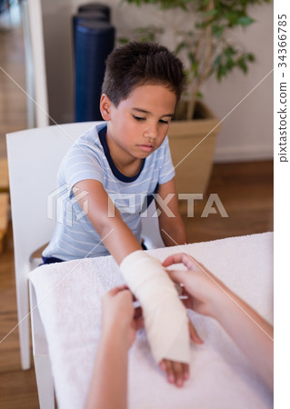 Boy looking at female therapist wrapping bandage on hand Boy looking at female therapist wrapping bandage on hand 34366785