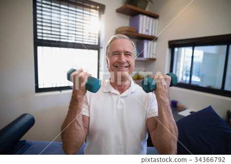 Portrait of smiling senior male patient holding dumbbells Portrait of smiling senior male patient holding dumbbells 34366792
