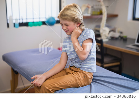 Boy sitting on bed with neck ache Boy sitting on bed with neck ache 34366810