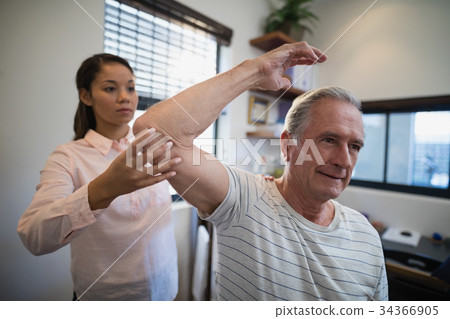 Female doctor examining elbow of male patient 34366905
