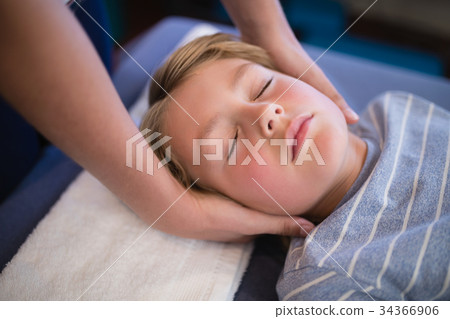 High angle view of boy with eyes closed receiving neck massage from female therapist 34366906