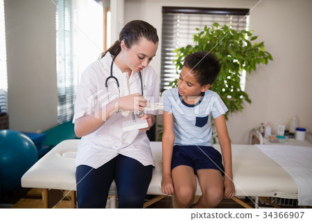 Young female therapist explaining boy with artificial bone while sitting on bed 34366907