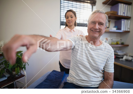 Portrait of smiling senior male patient sitting with female doctor examining shoulder 34366908