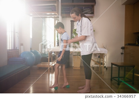 Side view of boy standing on stress balls with female therapist Side view of boy standing on stress balls with female therapist 34366957