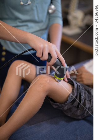 Midsection of female therapist using ultrasound machine on knee 34366966