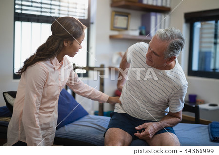 Female therapist examining back of male patient sitting on bed Female therapist examining back of male patient sitting on bed 34366999