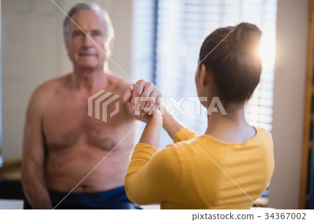 Rear view of female therapist giving arm massaging to senior male patient 34367002