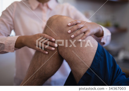 Midsection of female therapist examining knee with senior male patient 34367003
