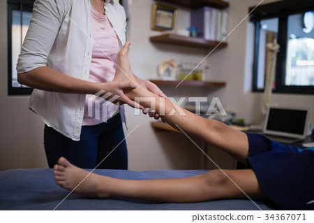 Young female therapist massaging sole of foot with boy on bed 34367071