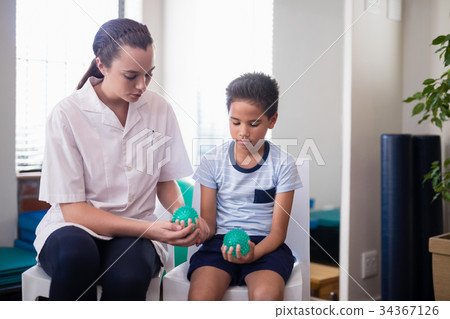 Female therapist sitting by boy on chairs with squeeze balls Female therapist sitting by boy on chairs with squeeze balls 34367126