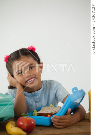 Schoolgirl sitting with tiffin box against white background Schoolgirl sitting with tiffin box against white background 34367127