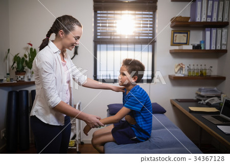 Side view of female therapist examining boy on bed Side view of female therapist examining boy on bed 34367128