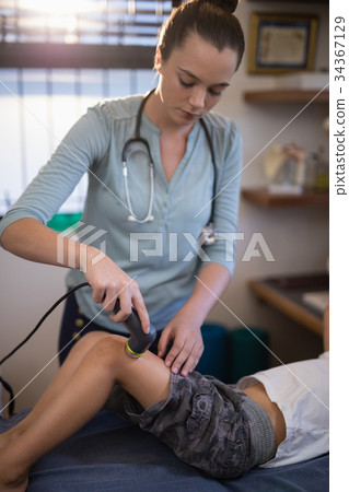 Young female therapist using ultrasound machine on knee of boy 34367129