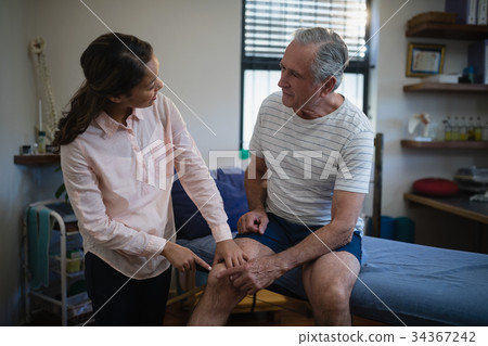 Female therapist pointing at knee while talking with senior male patient Female therapist pointing at knee while talking with senior male patient 34367242