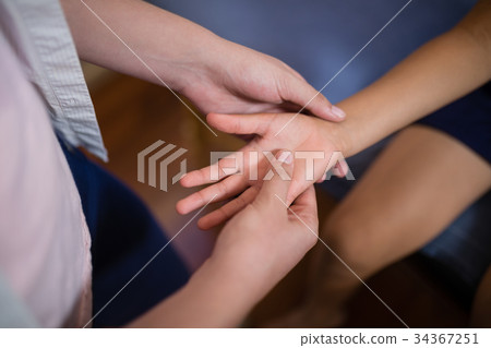 Midsection of female therapist massaging palm with boy sitting on bed 34367251