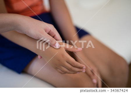 Close-up of female therapist examining hand while boy sitting on bed 34367424