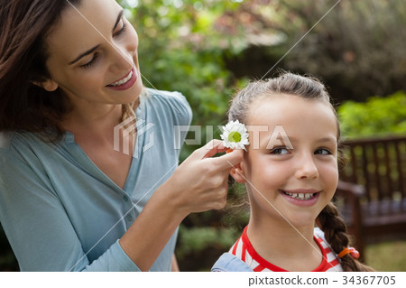 Smiling mother positioning white flower in hair of girl 34367705