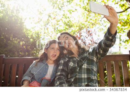 Low angle view of woman taking selfie with daughter while making faces against trees 34367834