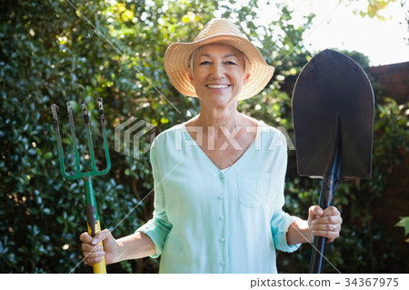 Portrait of smiling senior woman holding garden fork and shovel 34367975