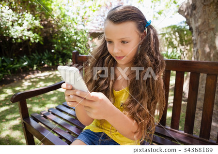 Girl using cellphone while sitting on wooden bench 34368189