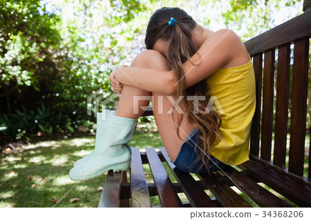 Side view of upset girl sitting on wooden bench Side view of upset girl sitting on wooden bench 34368206