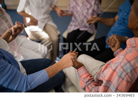 High angle view of seniors and female doctor holding hands while sitting on chairs High angle view of seniors and female doctor holding hands while sitting on chairs 34369465