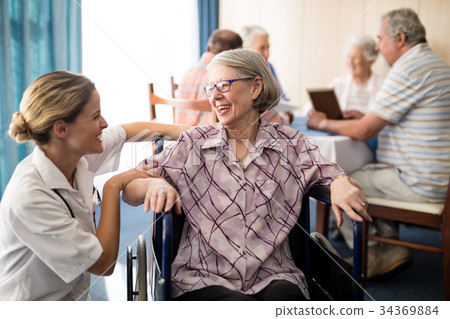 Cheerful disabled senior woman sitting on wheelchair looking at female doctor 34369884