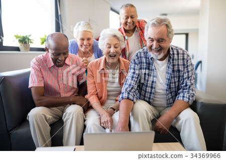 Cheerful senior friends looking at laptop on table 34369966
