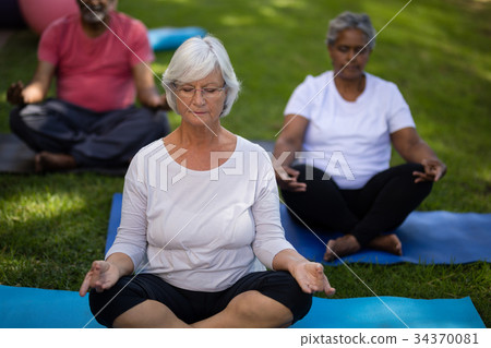 Senior woman with friends meditating at park Senior woman with friends meditating at park 34370081