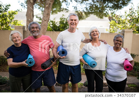 Portrait of laughing senior friends carrying exercise mats at park 34370107