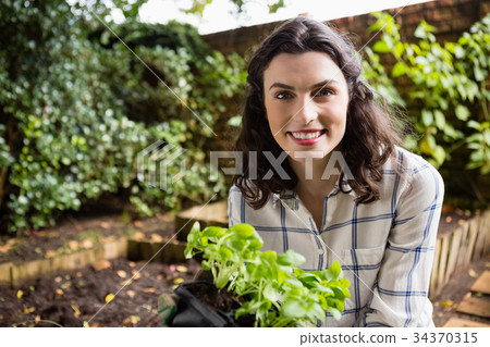 Smiling woman holding sapling plant in garden 34370315