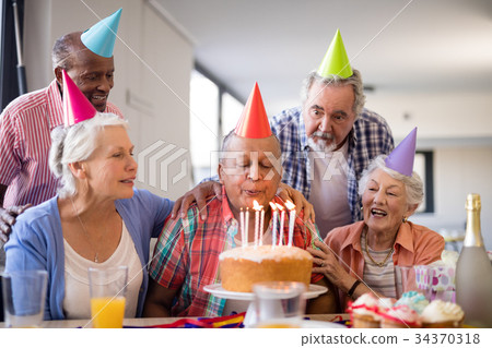 Friends looking at senior man blowing birthday candles 34370318