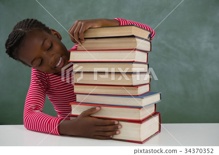 Schoolgirl sitting with books stack against chalkboard 34370352