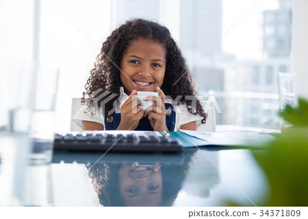 Portrait of smiling businesswoman holding coffee cup at desk 34371809