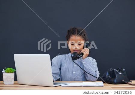 Businesswoman using landline phone while working on laptop Businesswoman using landline phone while working on laptop 34372026