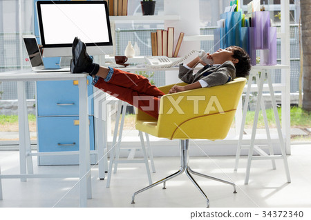 Businessman talking on landline phone while sitting on chair with feet up 34372340