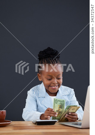 Businesswoman counting paper currency while using laptop 34372547