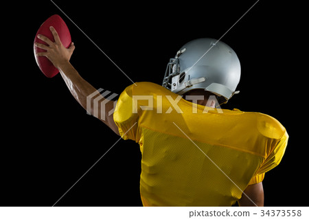 American football player holding a ball high in one hand 34373558