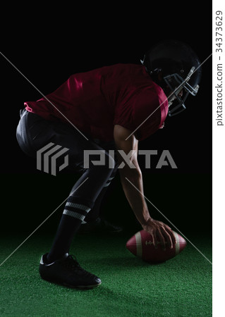 American football player bending holding a ball on turf with both his hands 34373629