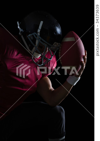 American football player sitting holding a ball in his hand 34373639