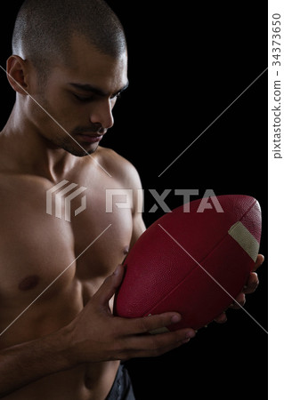 Muscular American football player looking at football in both his hands Muscular American football player looking at football in both his hands 34373650