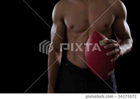 Muscular American football player holding a football in his hand 34373872