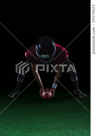 American football player bending holding a ball on turf with both his hands American football player bending holding a ball on turf with both his hands 34374023