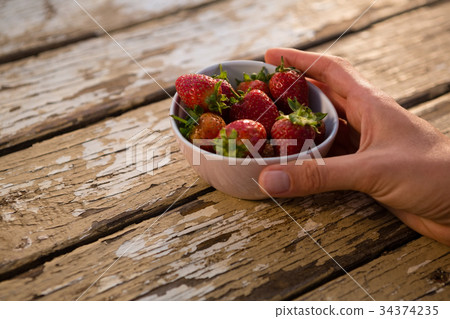 Cropped hand holding bowl containing strawberries 34374235