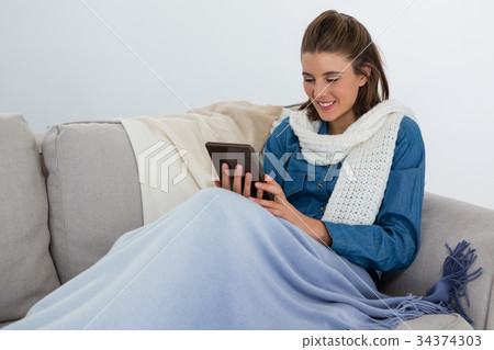 Smiling woman using tablet computer while sitting on sofa 34374303