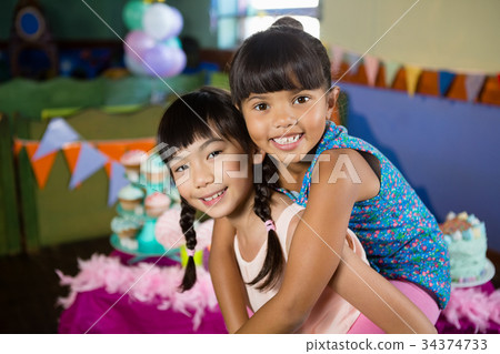 Girl giving piggyback ride to her friend during birthday party Girl giving piggyback ride to her friend during birthday party 34374733