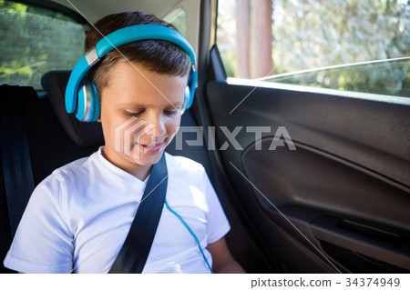 Teenage boy with headphones sitting in the back seat of car 34374949