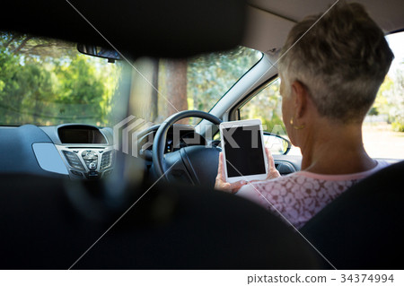 Senior woman using digital tablet while driving a car 34374994